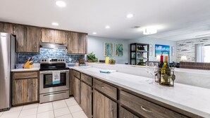 A modern kitchen with wooden cabinets, a stainless steel refrigerator, and a white countertop. - 3 min walk to beach! Ocean and river views. Great sunsets! Updated 2 br 2ba (Daytona Beach Shores)