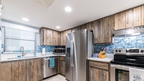 A modern kitchen with wooden cabinets, stainless steel appliances, a tiled backsplash, and a window with blinds. - 3 min walk to beach! Ocean and river views. Great sunsets! Updated 2 br 2ba (Daytona Beach Shores)