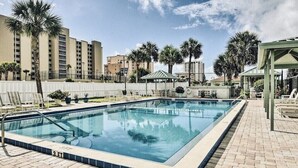 A rectangular swimming pool with a tiled edge, surrounded by lounge chairs and palm trees. - 3 min walk to beach! Ocean and river views. Great sunsets! Updated 2 br 2ba (Daytona Beach Shores)