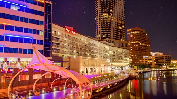 A hotel with a prominent 'Sheraton' sign, a waterfront location, and a modern bridge structure. - Green Castle Suite in Tampa (Tampa)