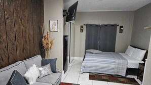 A modern bedroom with a grey sofa, a bed with a striped duvet, a small rug, and a wooden wall. - Green Castle Suite in Tampa (Tampa)