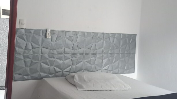 A bedroom with a bed, a patterned headboard, a bedside table, and a door leading to a balcony. - POUSADA MORADAS (Aracaju)