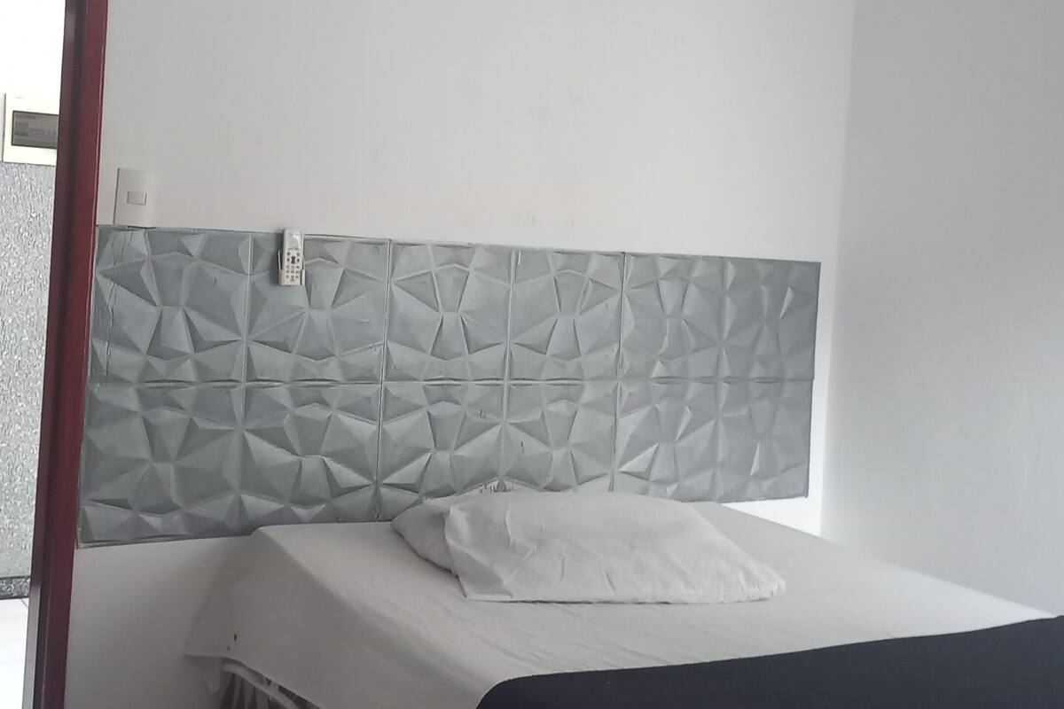 A bedroom with a bed, a patterned headboard, a bedside table, and a door leading to a balcony.