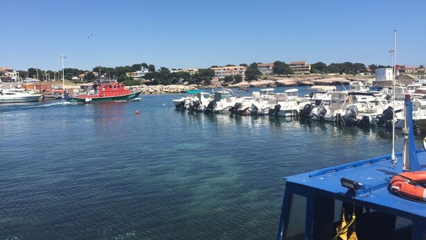 A marina with boats docked, a red boat in the foreground, and buildings in the background.