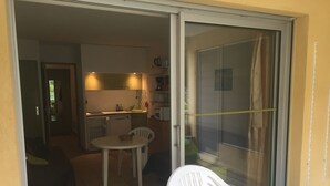 A small, open-plan living space with a kitchenette, a dining area with a table and chairs, and a sliding glass door leading to a balcony.