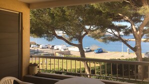 A balcony with a view of the sea, trees, and parked cars.