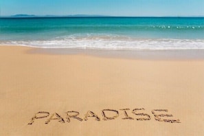 Una playa con la palabra "PARADISE" escrita en la arena.
