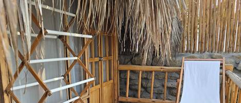 A wooden deck with a drying rack, a wooden chair with a white cushion, and a thatched roof structure.