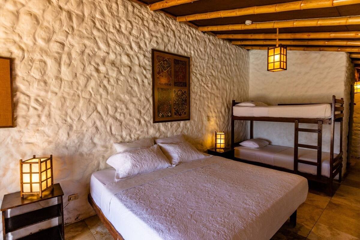 Une chambre confortable avec un lit superposé, un lit simple et un mur à texture. Il y a deux tables de chevet avec des lampes.