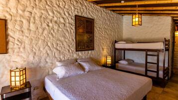 A cozy room with a bunk bed, a single bed, and a textured wall. There are two bedside tables with lamps.