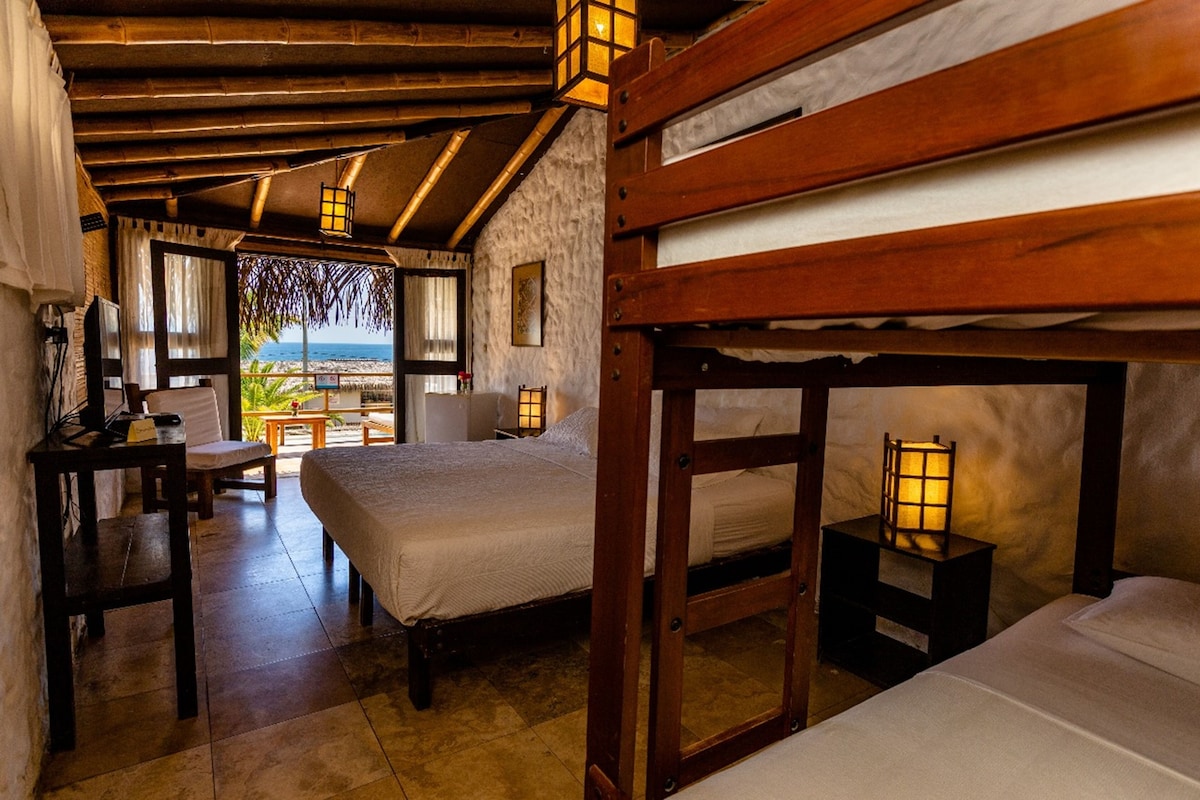 A room with a bed, a nightstand, a table, and a view of the beach.