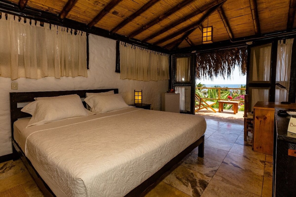 Une chambre avec un grand lit, un plafond en bois et un balcon offrant une vue sur l’océan.