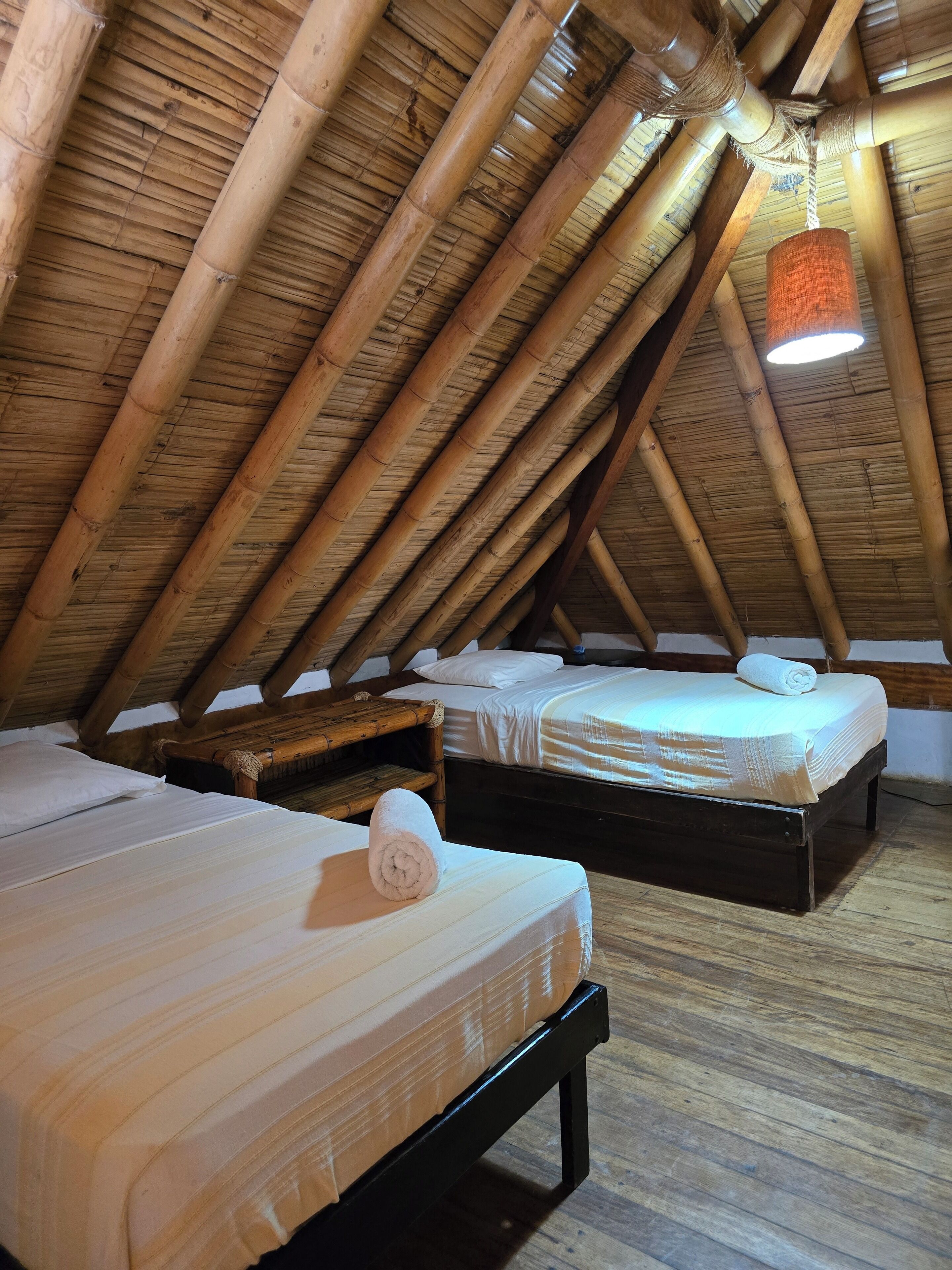 A cozy attic room with two beds, wooden beams, and a hanging light fixture.