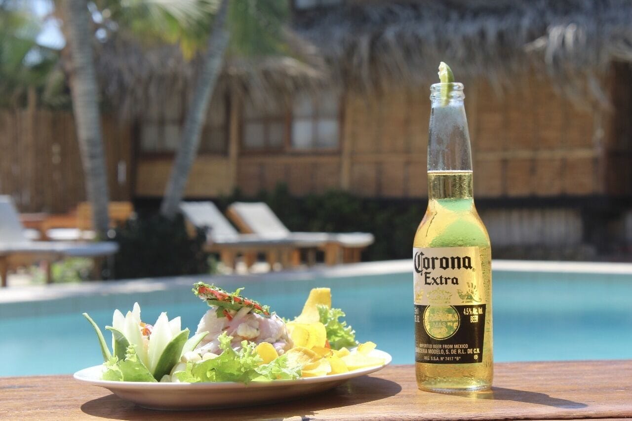 Une bouteille de bière Corona Extra à côté d’une assiette de nourriture, près d’une piscine.