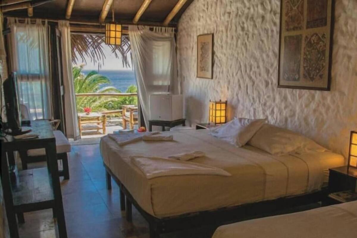 Une chambre à coucher comprenant un lit, des tables de chevet, une commode, une fenêtre avec des rideaux et une vue sur l’extérieur.