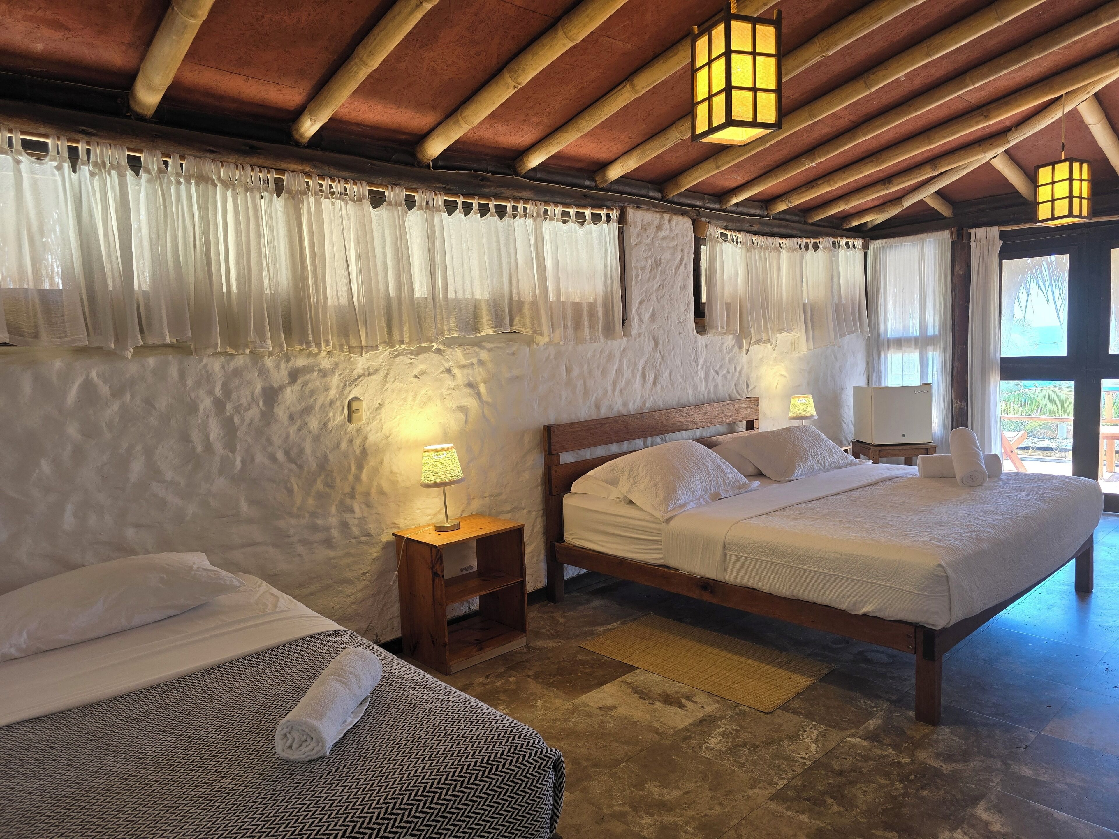Habitación de hotel con dos camas, techo de madera y vistas al exterior.