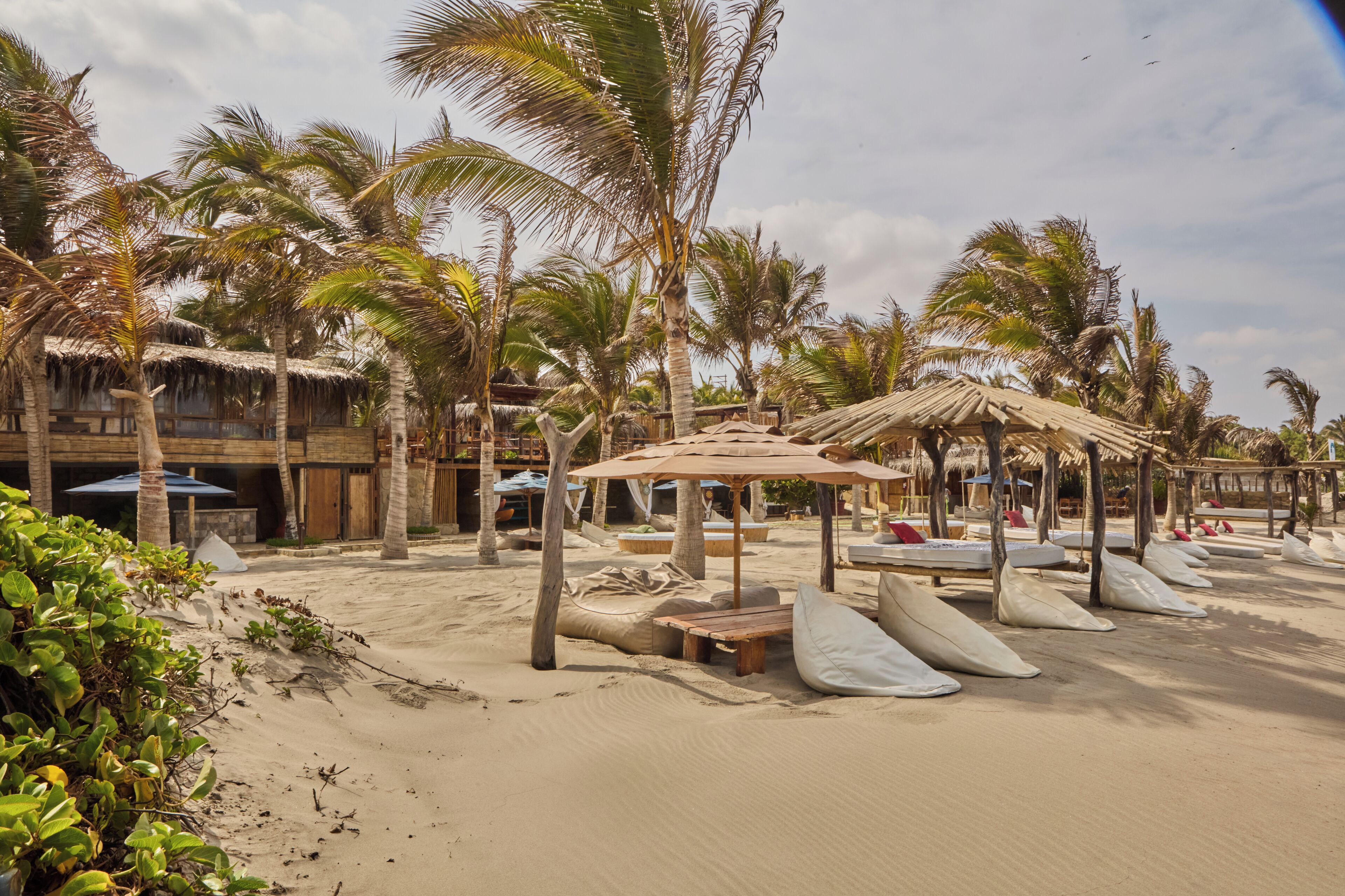 A beachside resort with thatched-roof huts, palm trees, and beach chairs.