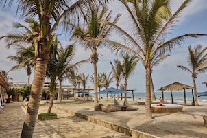 A beach with palm trees, a thatched-roof structure, and a sandy area with seating.