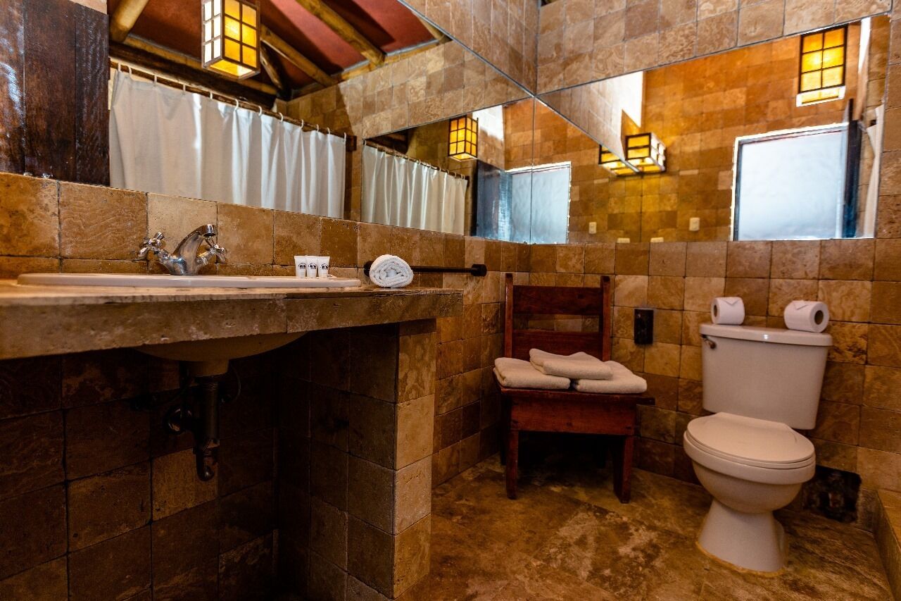 A bathroom with a stone-tiled wall, a wooden bench, a toilet, and a sink with a faucet.