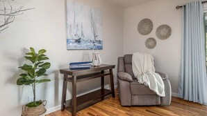 A living room with a grey sofa, a small table with decorative items, a potted plant, and wall art depicting sailboats. - Orange Door (Sparks)