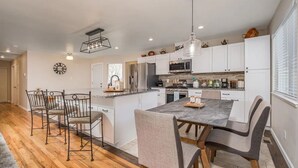 A modern kitchen with white cabinets, a central island, and a dining area with metal chairs. - Orange Door (Sparks)