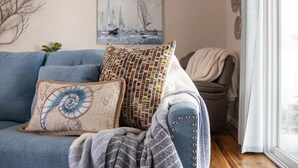 A cozy living room with a blue sofa, decorative pillows, a blanket, and a painting of sailboats on the wall. - Orange Door (Sparks)