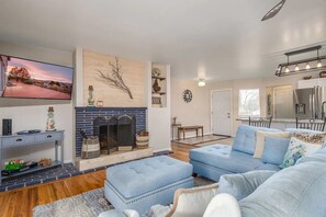 A modern living room with a fireplace, blue sofas, a flat-screen TV, and a kitchen in the background. - Orange Door (Sparks)