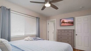A bedroom with a bed, a ceiling fan, a dresser, and a door. - Orange Door (Sparks)