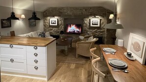 A cozy living room with a stone fireplace, a television, and a dining area with a wooden table set for two. - Cosy & elegant cottage in charming Newlyn (Penzance)