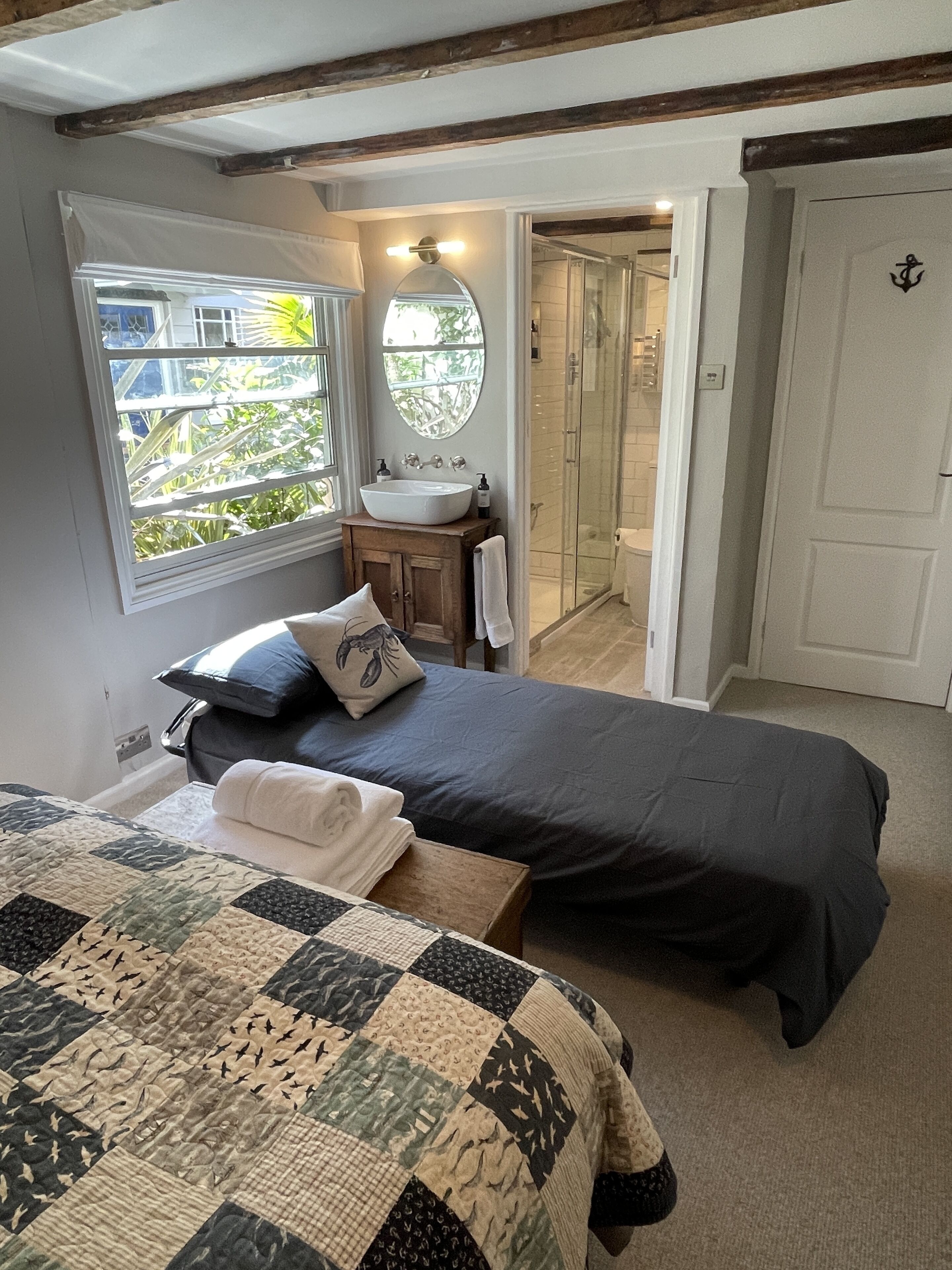 A bedroom with a bed, a bedside table with a lamp, a window with a view of greenery, and a bathroom with a shower and sink.