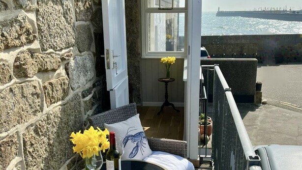 A stone wall, a wicker chair, a small table with a vase of yellow flowers, and a view of the sea. - Cosy & elegant cottage in charming Newlyn (Penzance)