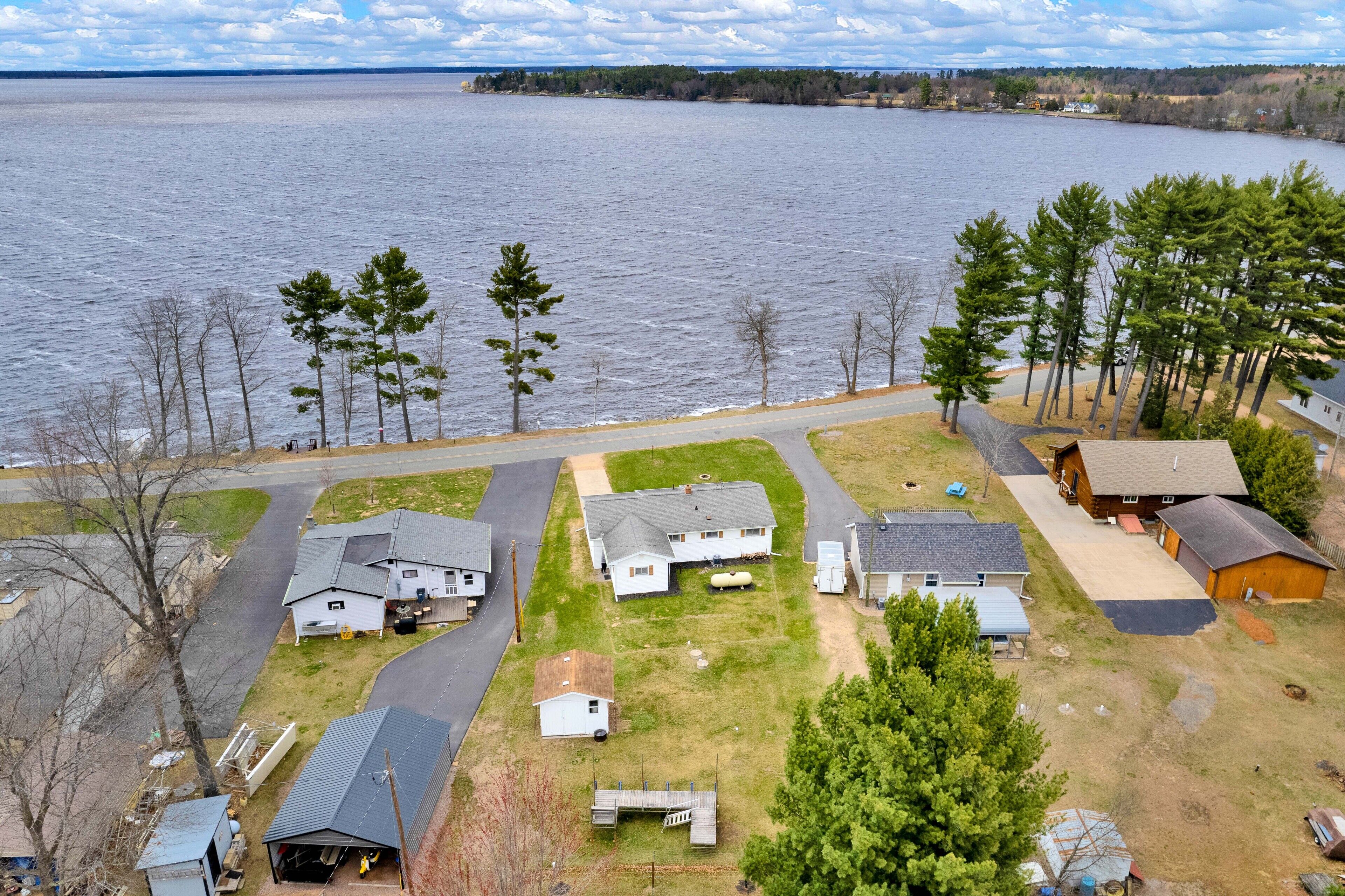 A residential area with houses near a large body of water, featuring a mix of single and multi-story buildings, a road, and a grassy area with trees.