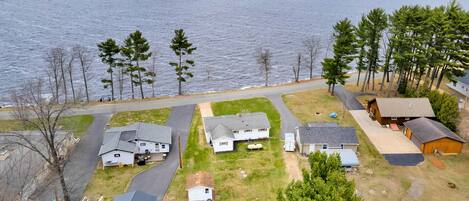 A residential area with houses near a large body of water, featuring a mix of single and multi-story buildings, a road, and a grassy area with trees.