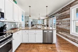 A spacious kitchen with white cabinetry, a stainless steel dishwasher, and a wooden floor.