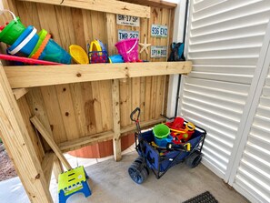Een houten opbergruimte met labels op de bakken, een blauwe kinderwagen en een klein krukje.