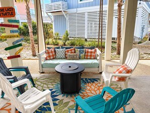 A beachside seating area with a swing, a sofa with colorful cushions, and a signpost with various directional signs.