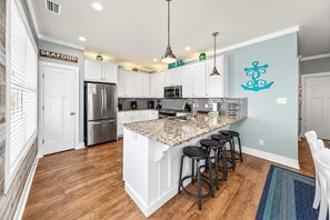 A modern kitchen with white cabinetry, a stainless steel refrigerator, a granite countertop, and a bar area with stools.