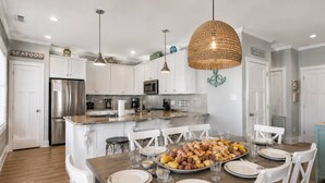 A modern kitchen with white cabinets, stainless steel appliances, and a dining area with a wooden table set for six.