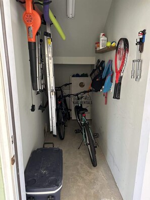 A narrow garage with bicycles, a lawnmower, and a sign for a bike rental service.