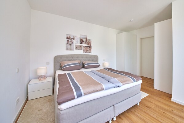 Une chambre à coucher avec un lit, des tables de chevet, un mur décoré de tableaux et une porte.