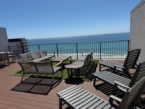 A balcony with outdoor furniture, a view of the ocean, and a building in the background.