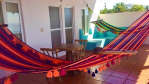 Una hamaca instalada entre dos puertas en un patio con baldosas, con una mesa y sillas cerca.