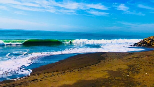 Una playa con olas, cielo despejado y una zona rocosa.