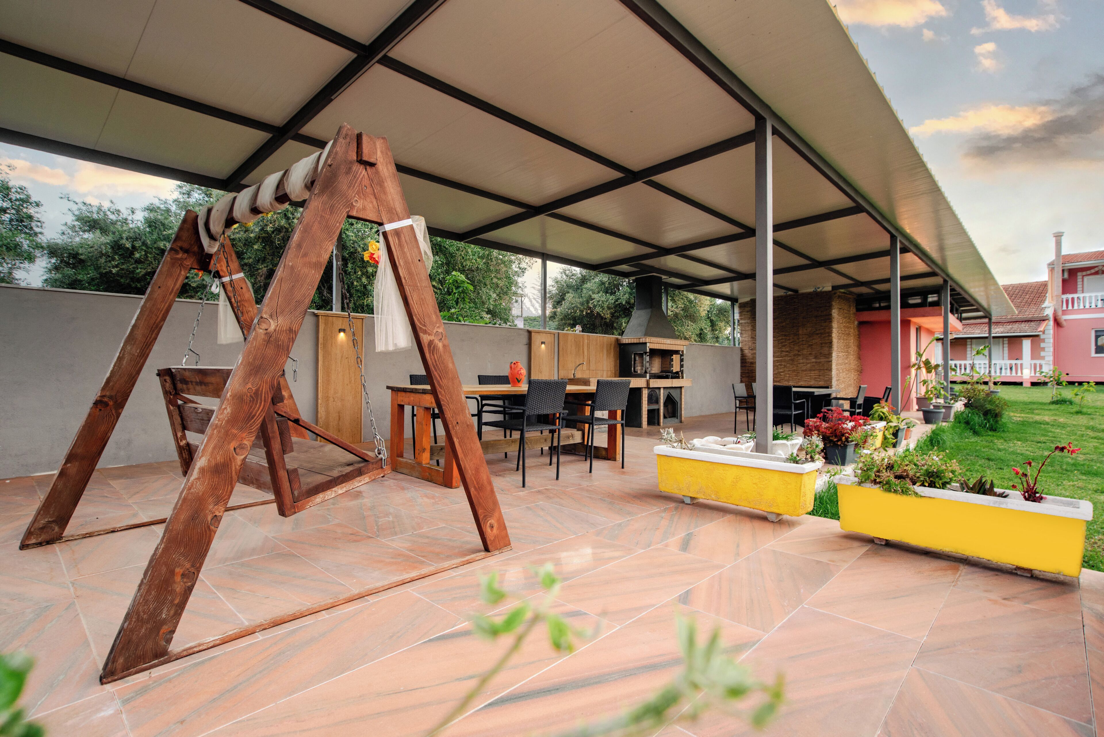 Une terrasse extérieure avec une balançoire, un coin repas et un jardinier jaune orné de fleurs.
