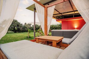A tented outdoor area with a wooden table and a cushioned seating area, surrounded by greenery and a red wall. - Riposo Studios and Apartments (Corfu)