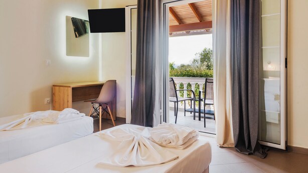Habitación de hotel con dos camas, un escritorio, una silla, un televisor y un balcón con cortinas.