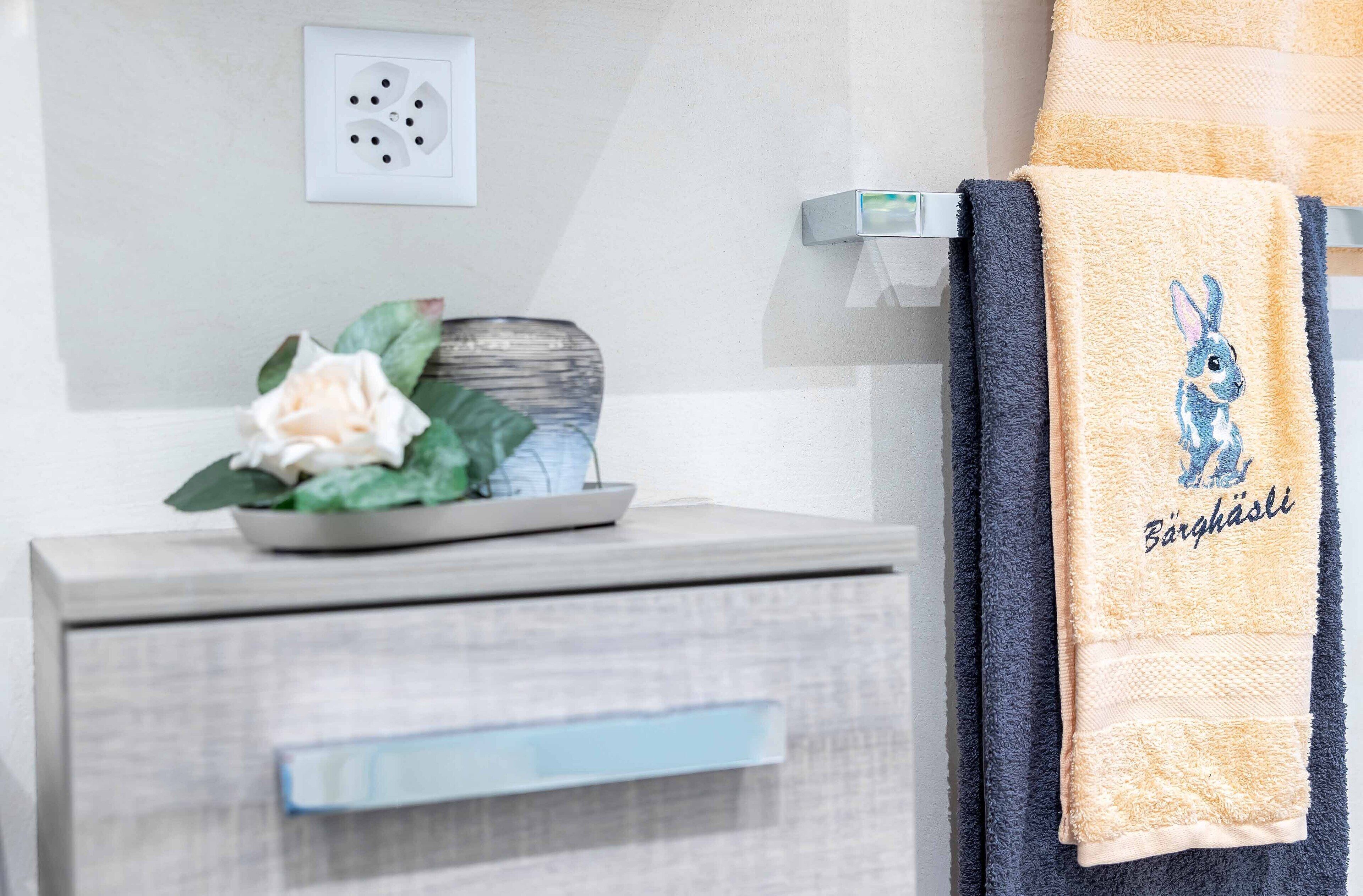 A bathroom with a towel rack holding a yellow towel with a bunny design and the text "Bergäste".