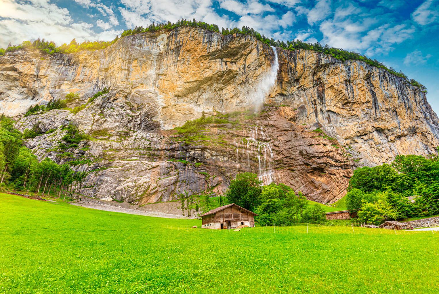 Ein Berg mit einem Wasserfall und einer kleinen Hütte in einem grünen Feld.