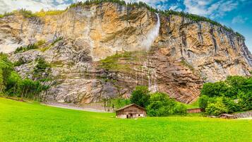 Ein Berg mit einem Wasserfall und einer kleinen Hütte in einem grünen Feld.
