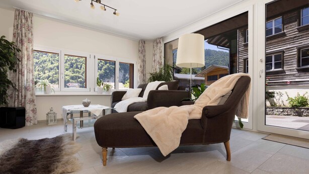 Ein modernes Wohnzimmer mit einer braunen Couch, einem großen Fenster und Blick auf ein Holzgebäude.